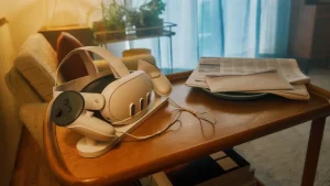 Un casque de réalité virtuelle Meta Quest posé sur son socle de recharge à côté de ses manettes, sur une table basse en bois avec du courrier et un journal, symbolisant l'abandon du métavers social Horizon Worlds en VR.