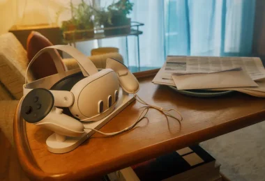 Un casque de réalité virtuelle Meta Quest posé sur son socle de recharge à côté de ses manettes, sur une table basse en bois avec du courrier et un journal, symbolisant l'abandon du métavers social Horizon Worlds en VR.