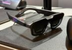 unettes AR gaming ASUS ROG Xreal R1 posées sur un tapis de souris noir avec LED RGB rose et bleu sur la branche, manette ROG en arrière-plan et station d'accueil Control Dock visible, premier modèle de lunettes display 240 Hz micro-OLED au monde.
