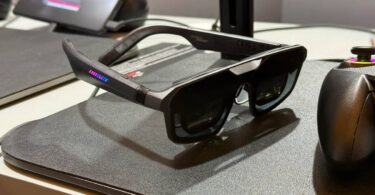unettes AR gaming ASUS ROG Xreal R1 posées sur un tapis de souris noir avec LED RGB rose et bleu sur la branche, manette ROG en arrière-plan et station d'accueil Control Dock visible, premier modèle de lunettes display 240 Hz micro-OLED au monde.