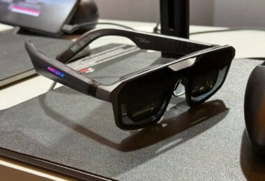 unettes AR gaming ASUS ROG Xreal R1 posées sur un tapis de souris noir avec LED RGB rose et bleu sur la branche, manette ROG en arrière-plan et station d'accueil Control Dock visible, premier modèle de lunettes display 240 Hz micro-OLED au monde.