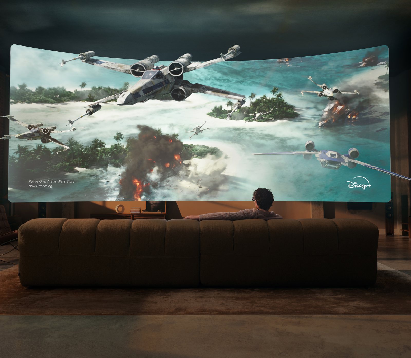 Homme assis sur un canapé portant les Meta VR Glasses devant un écran virtuel géant et incurvé diffusant Rogue One sur Disney+, affiché par-dessus le salon réel en réalité mixte
