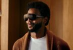 Meta VR Glasses portées par un homme en gilet en maille marron : lunettes de réalité virtuelle de 100 g à visière noire enveloppante, branches fines et câble optique relié au boîtier de calcul